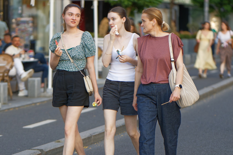 22 - Two girls and a woman walking casually down a city street while eating ice cream